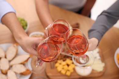 Photo of People clinking glasses with rose wine at wooden table, above view