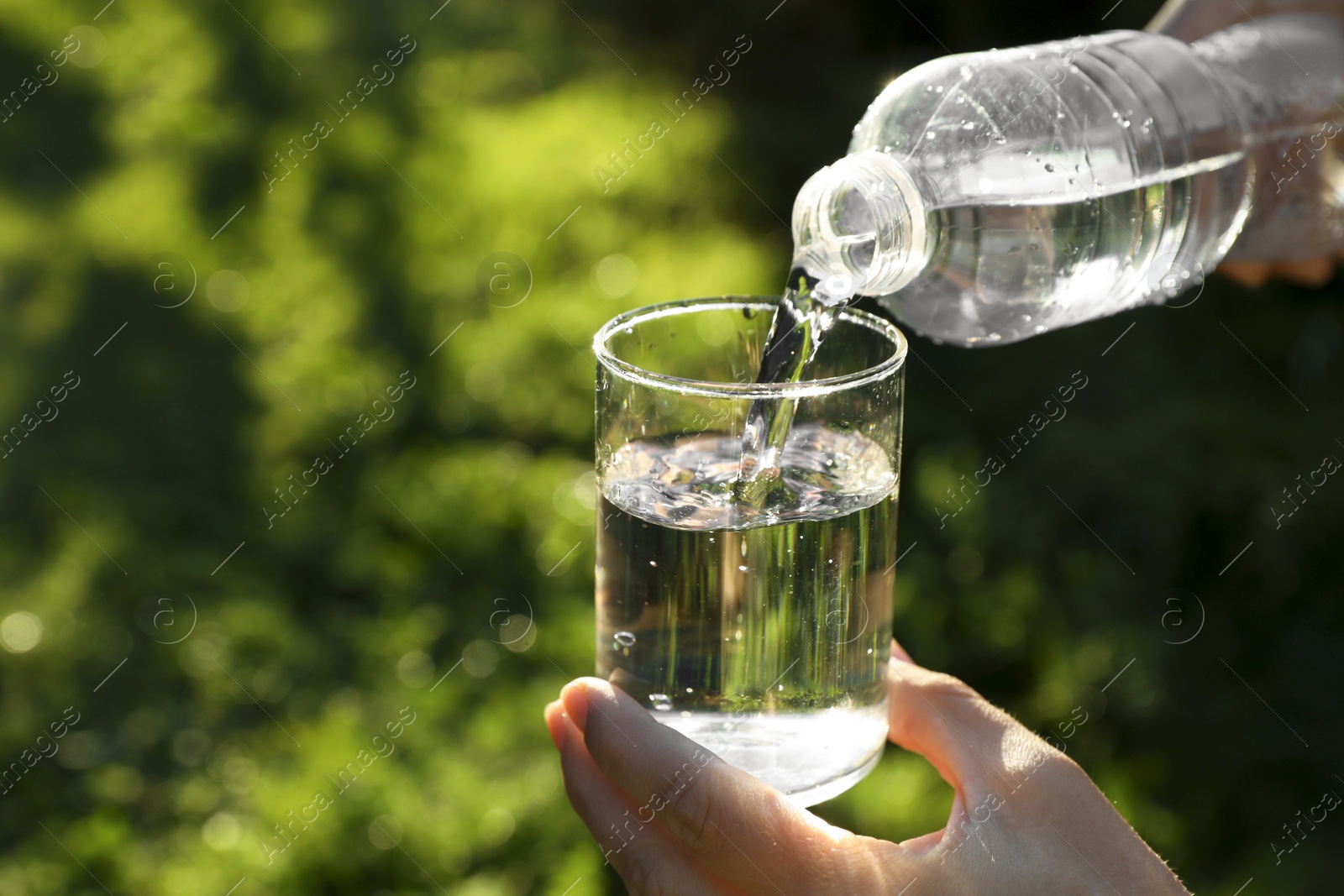 Photo of Man pouring fresh water from bottle into glass outdoors, closeup. Space for text