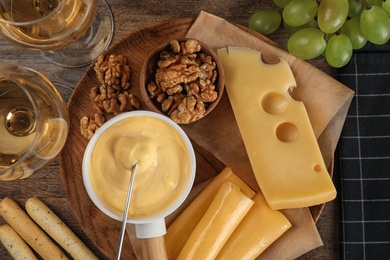 Flat lay composition with pot of tasty cheese fondue and products on wooden table