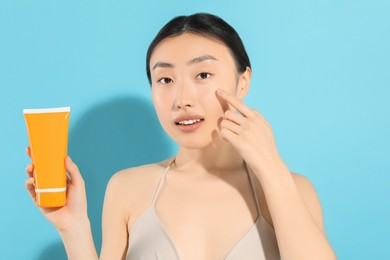 Beautiful young woman holding sun protection cream on light blue background