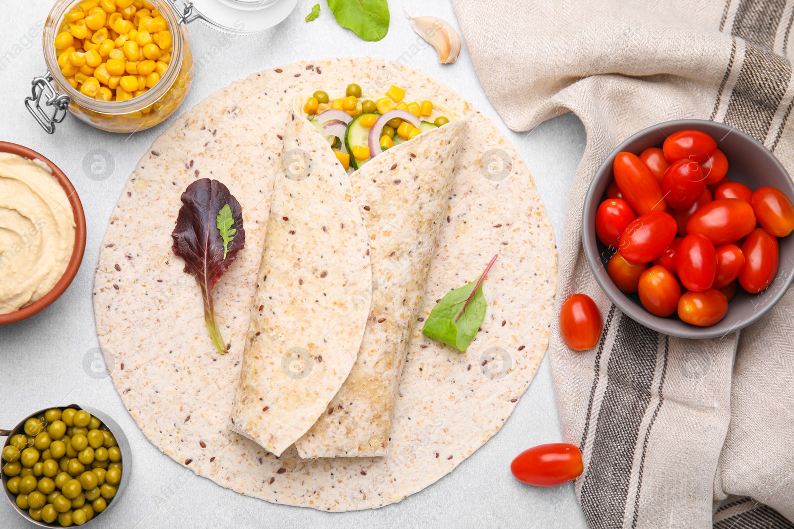 Photo of Delicious hummus wrap with vegetables on light table, flat lay