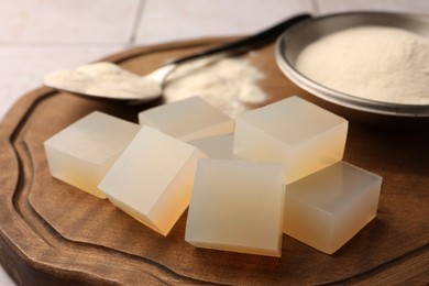 Photo of Agar-agar jelly cubes and powder on wooden board, closeup
