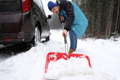 Photo of Man cleaning snow with shovel near stuck car outdoors