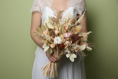 Photo of Bride holding beautiful dried flower bouquet on green background, closeup