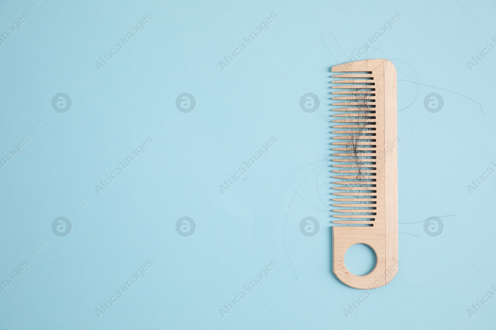 Photo of Wooden comb with lost hair on light blue background, top view. Space for text