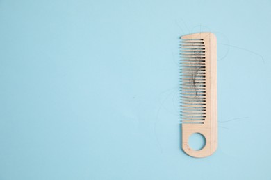 Wooden comb with lost hair on light blue background, top view. Space for text