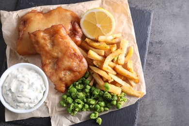 Photo of Tasty fish, chips, sauce and peas on grey table, top view
