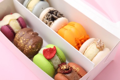 Photo of Cardboard box with delicious macarons on pink table, closeup
