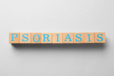 Photo of Word Psoriasis made of wooden cubes with letters on light grey background, top view
