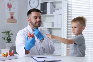 Photo of Endocrinologist showing thyroid gland model to little patient at table in hospital