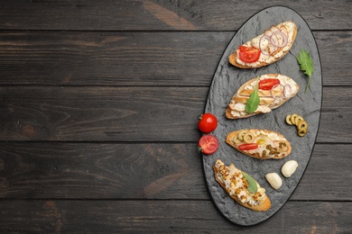 Photo of Slate plate of delicious chicken bruschettas on wooden table, top view. Space for text