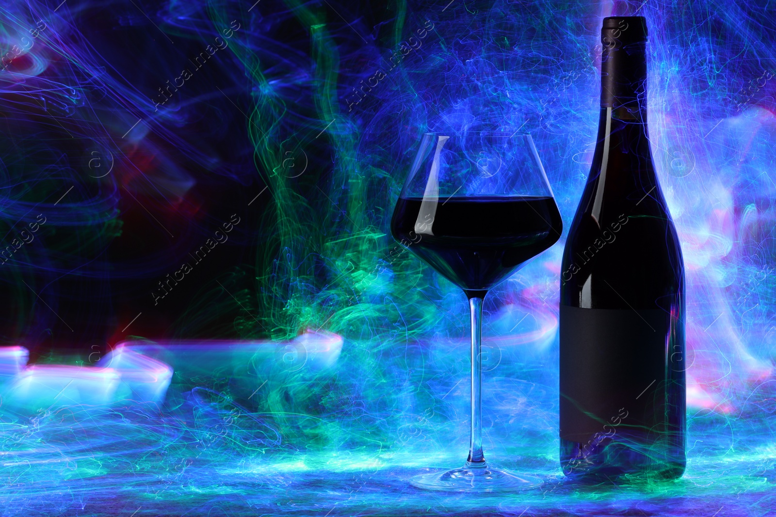 Photo of Red wine in glass and bottle in color lights, space for text