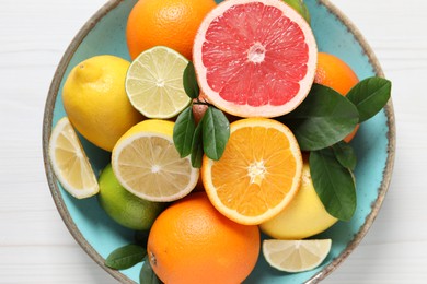 Different cut and whole citrus fruits on white wooden table, top view