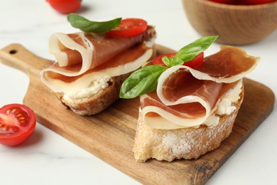 Photo of Tasty sandwiches with cured ham, basil and tomatoes on white table, closeup