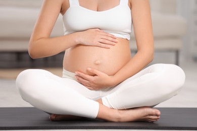 Photo of Pregnant woman sitting on yoga mat at home, closeup