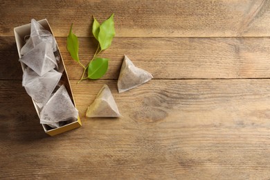 Photo of Box with paper tea bags and leaves on wooden table, flat lay. Space for text