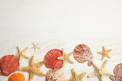 Photo of Beautiful sea stars, shells and sand on white wooden background, flat lay. Space for text