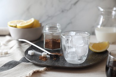 Photo of Cooking iced coffee. Ice cubes in glass, ingredients and spoon on white wooden table, closeup