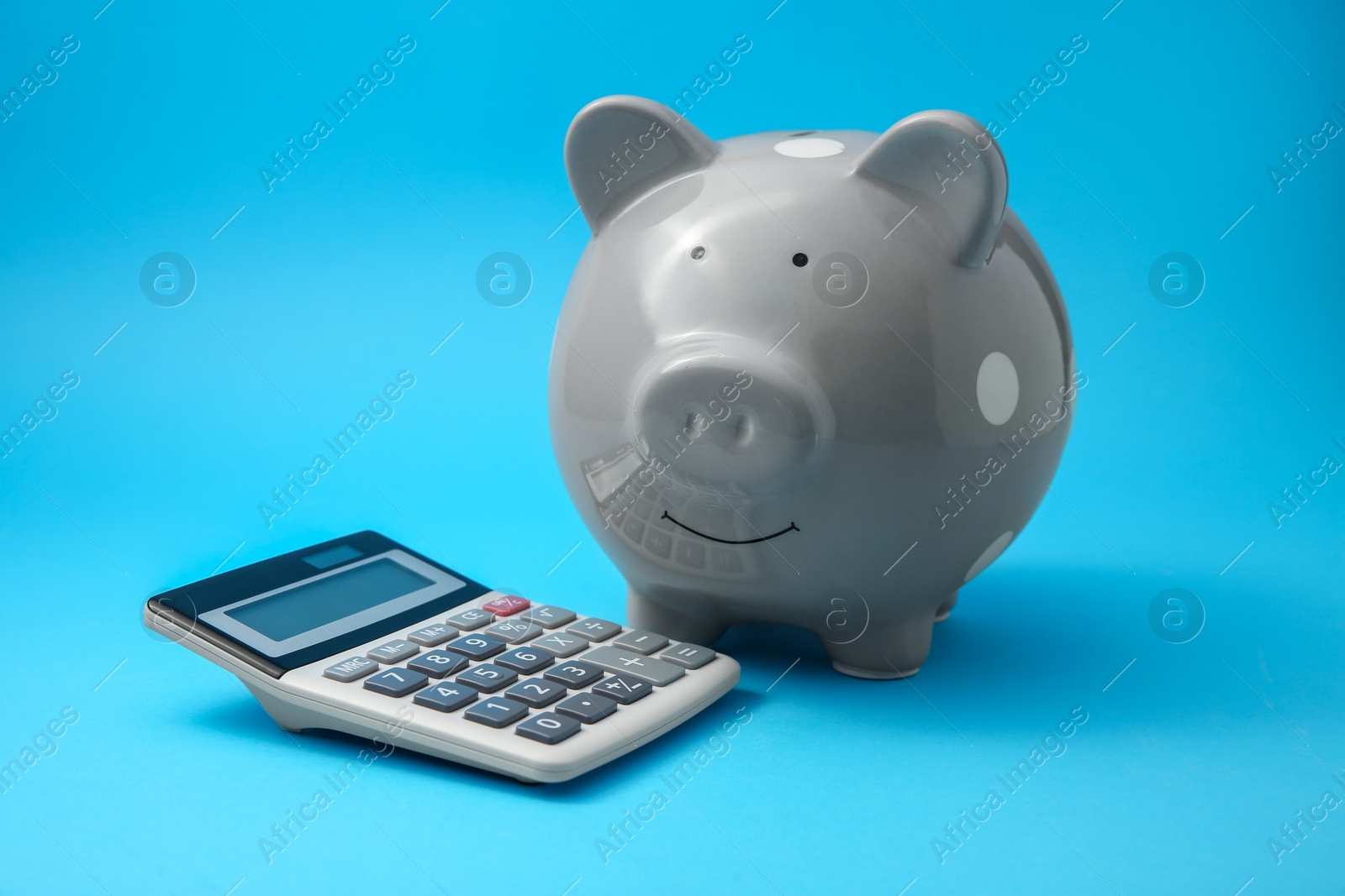 Photo of Piggy bank and calculator on light blue background