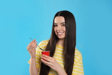 Photo of Happy teenage girl with delicious yogurt and spoon on light blue background