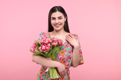 Happy young woman with beautiful bouquet on dusty pink background