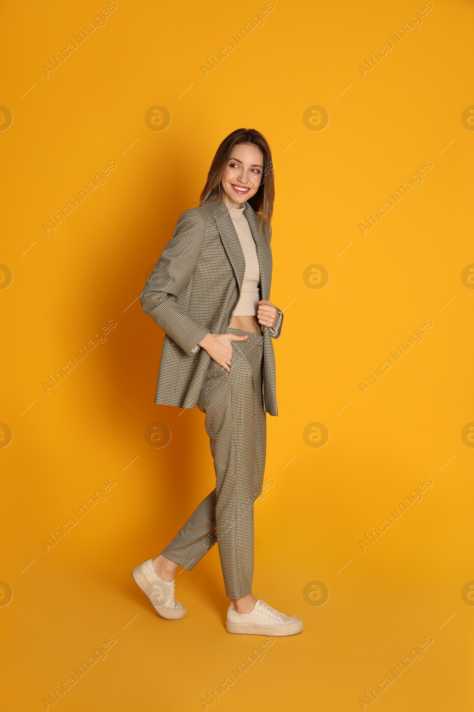 Photo of Full length portrait of beautiful young woman in fashionable suit on yellow background. Business attire