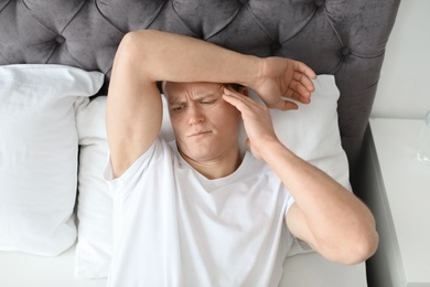 Photo of Young man with headache lying in bed