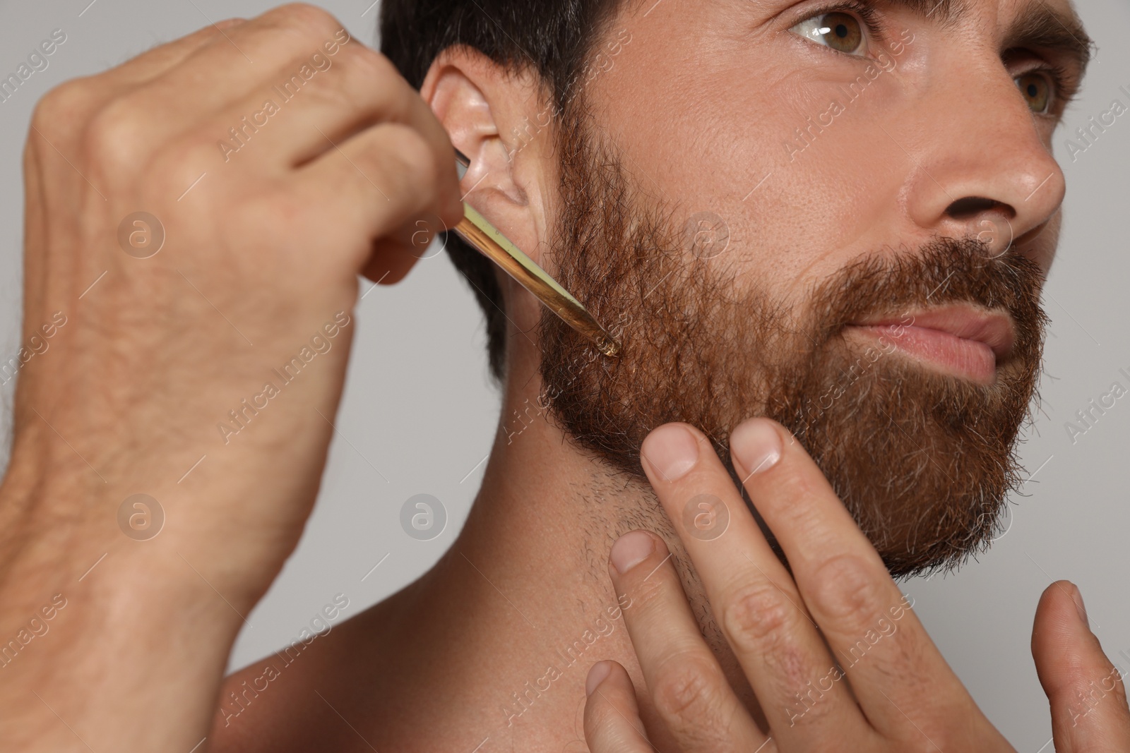 Photo of Man applying oil onto beard on grey background, closeup
