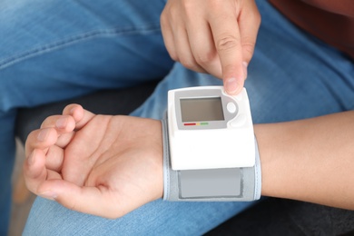 Photo of Young man checking pulse with blood pressure monitor on wrist, closeup