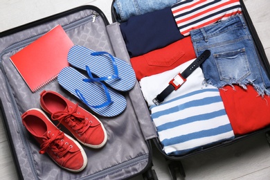 Packed suitcase with stuff on wooden background, top view