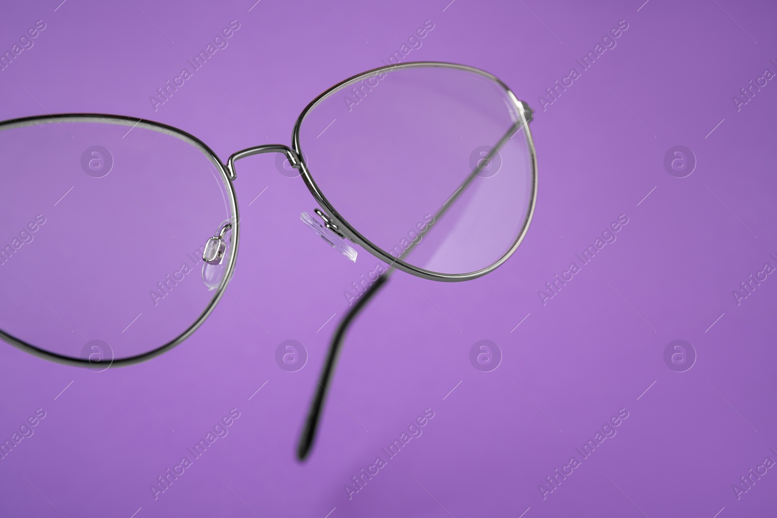 Photo of Stylish pair of glasses with metal frame on purple background, closeup