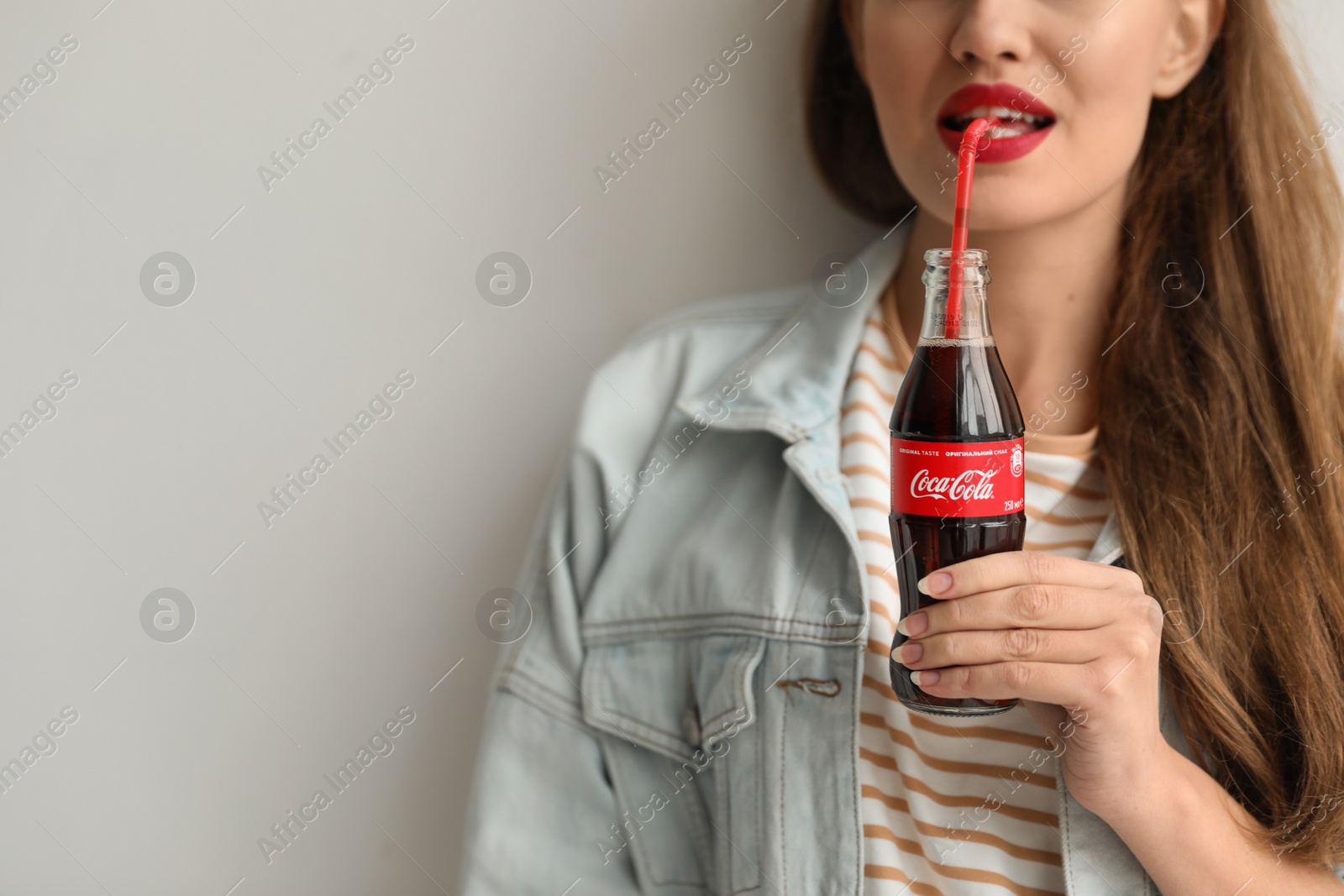 Photo of MYKOLAIV, UKRAINE - NOVEMBER 28, 2018: Young woman with bottle of Coca-Cola on light background, closeup. Space for text