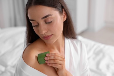 Photo of Young woman applying aloe gel from leaf onto her shoulder indoors