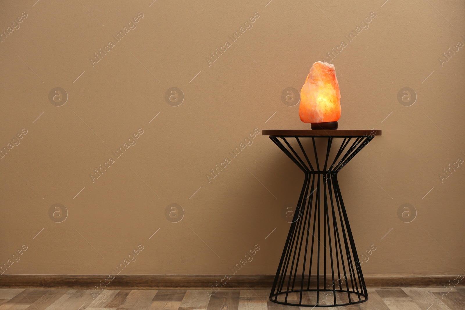 Photo of Himalayan salt lamp on table against  beige wall. Space for text