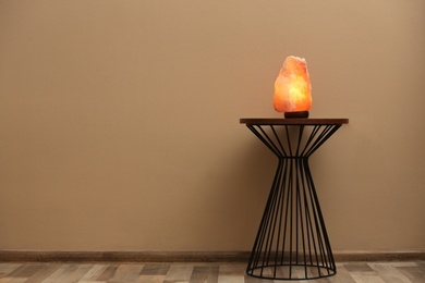 Himalayan salt lamp on table against  beige wall. Space for text