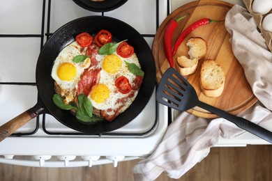 Delicious fried eggs with bacon and tomatoes in pan on stove, top view