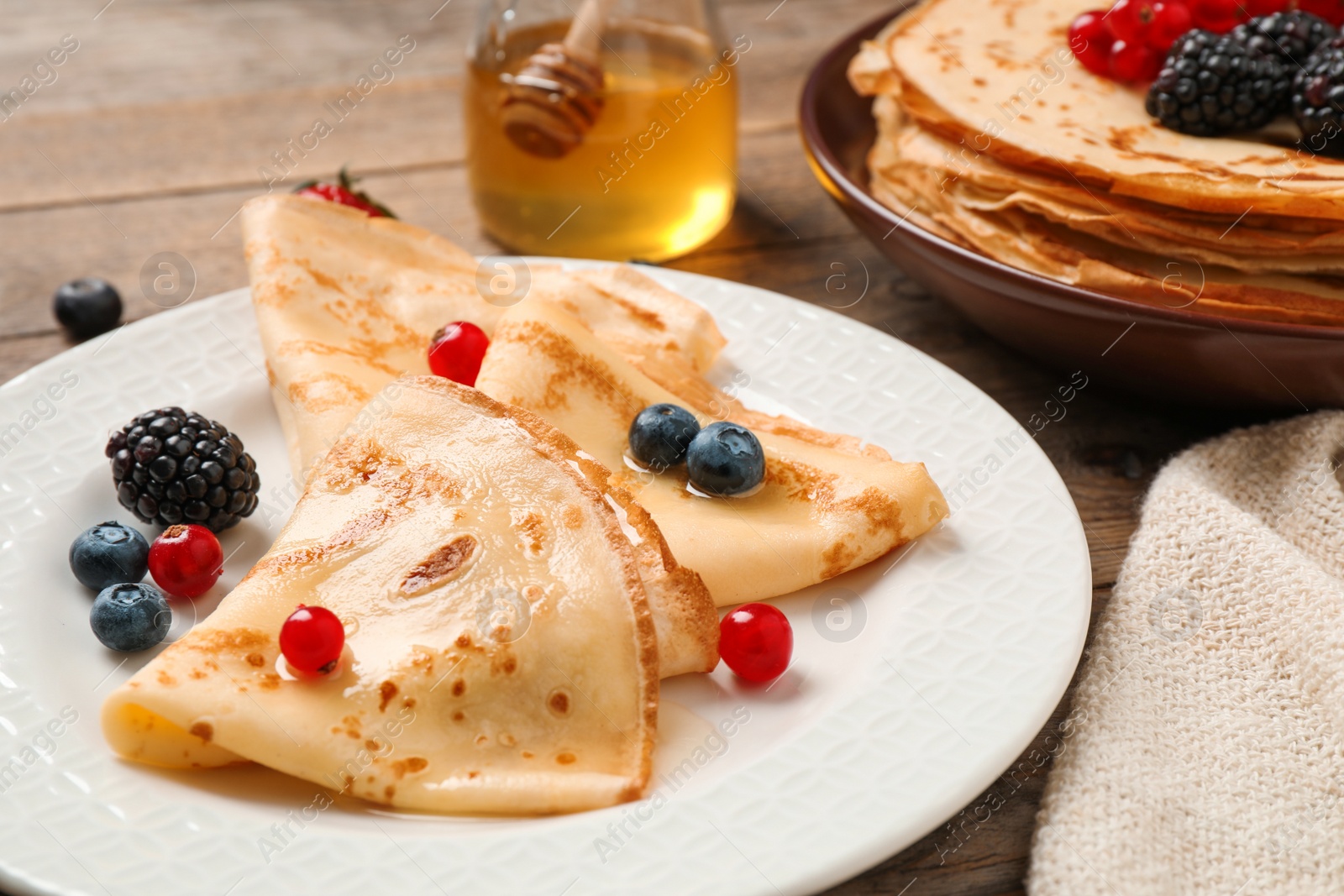 Photo of Delicious thin pancakes with berries on wooden table, closeup