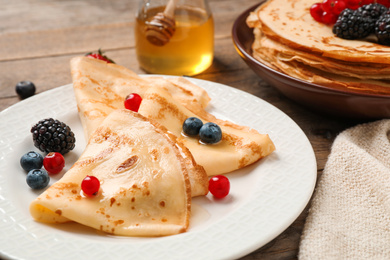 Delicious thin pancakes with berries on wooden table, closeup