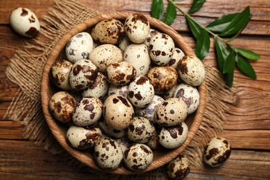 Photo of Bowl with quail eggs and green leaves on wooden table, flat lay