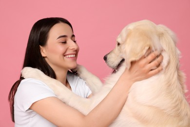 Photo of Happy woman playing with cute Labrador Retriever dog on pink background. Adorable pet