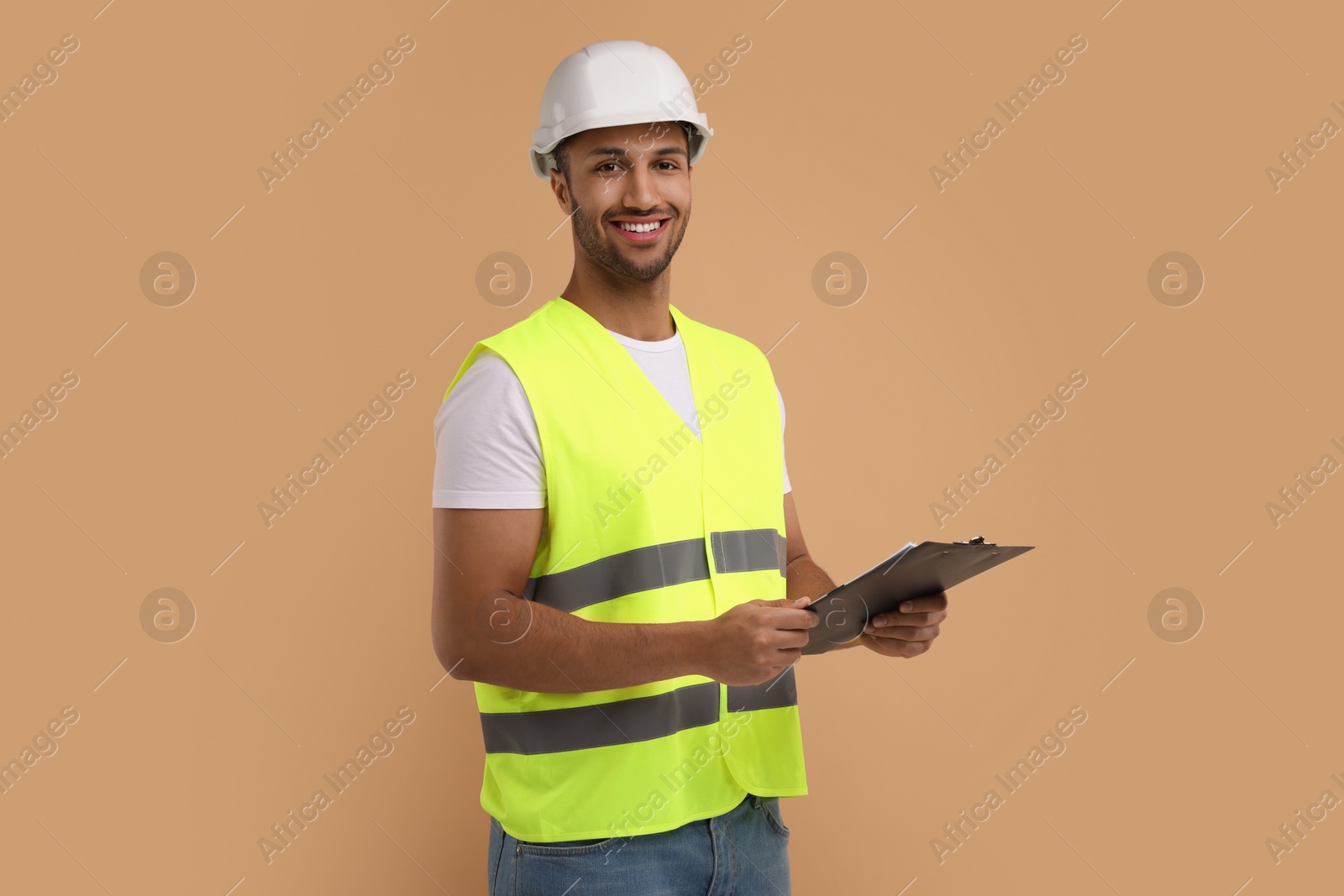 Photo of Engineer in hard hat holding clipboard on beige background