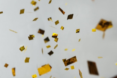 Photo of Shiny golden confetti falling down on light grey background