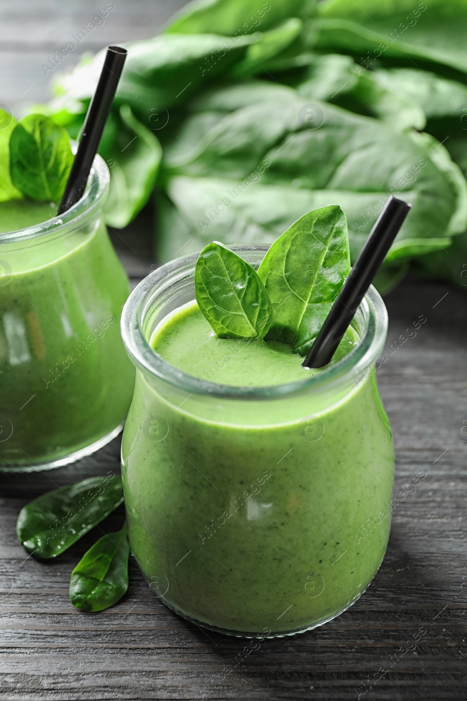 Photo of Jars of healthy green smoothie with fresh spinach on grey wooden table, closeup