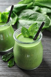 Jars of healthy green smoothie with fresh spinach on grey wooden table, closeup