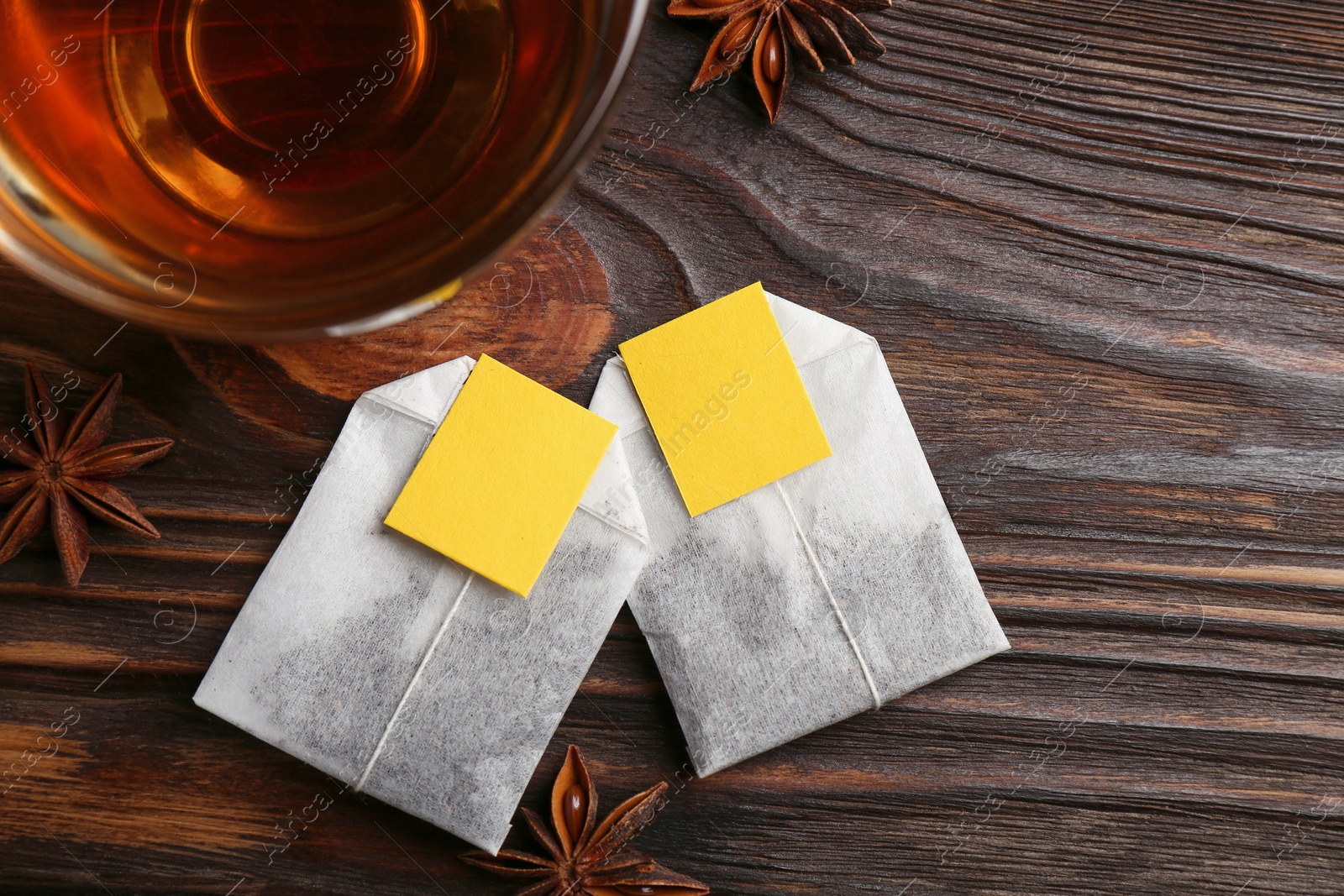 Photo of Tea bags, cup of hot drink and anise stars on wooden table, flat lay