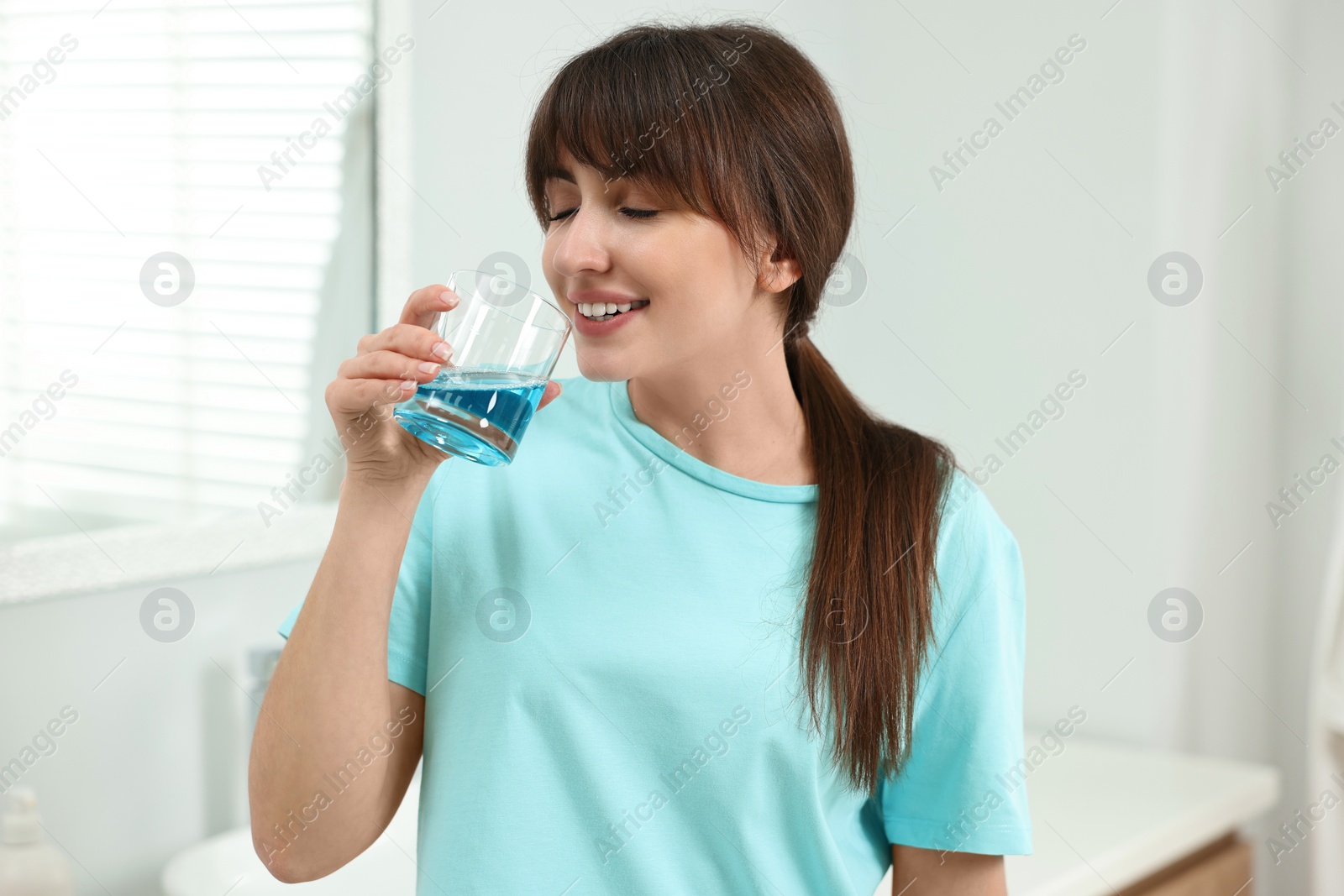 Photo of Young woman using mouthwash in bathroom. Oral hygiene