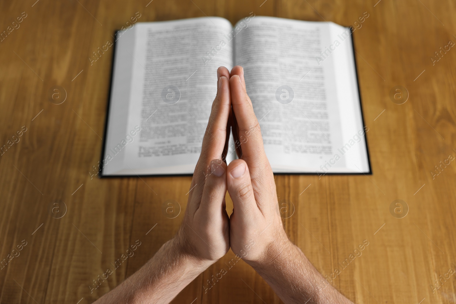 Photo of Man with Bible praying at wooden table, closeup