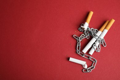 Photo of Cigarettes and chain on red background, flat lay with space for text. Quitting smoking concept