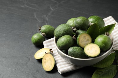 Fresh green feijoa fruits in bowl on black table, space for text