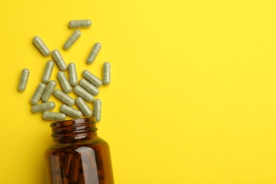 Photo of Vitamin pills and bottle on yellow background, top view. Space for text